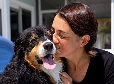 An Australian shepherd dog nuzzles her owner as they sit by the side of a pool.