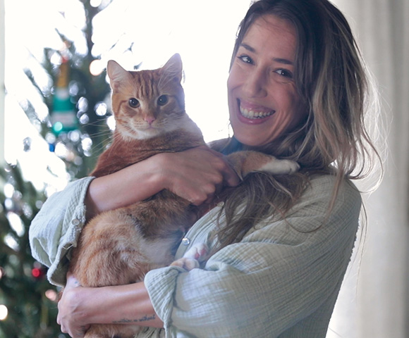 A woman smiles while hugging an orange and white cat.