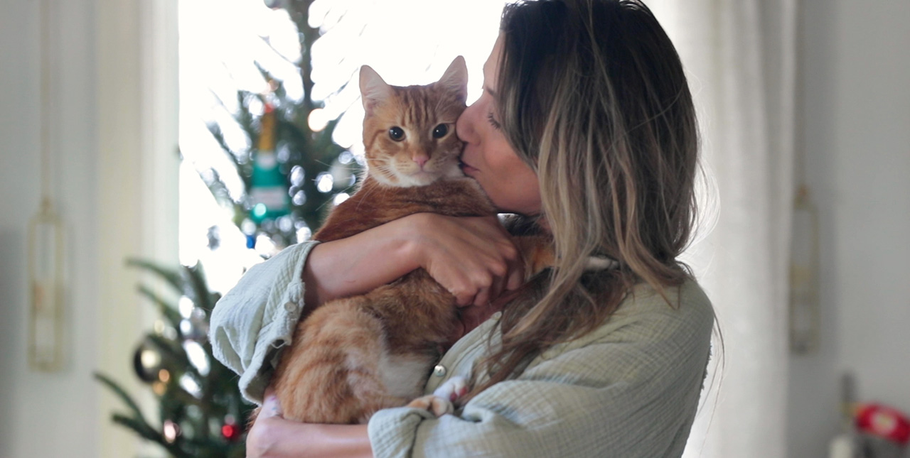 A woman hugs an orange and white cat while giving it a kiss on its cheek.