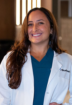 Dr. Mia Felix smiles for a headshot in the lobby of BluePearl. She is wearing turquoise scrubs and her whitecoat.