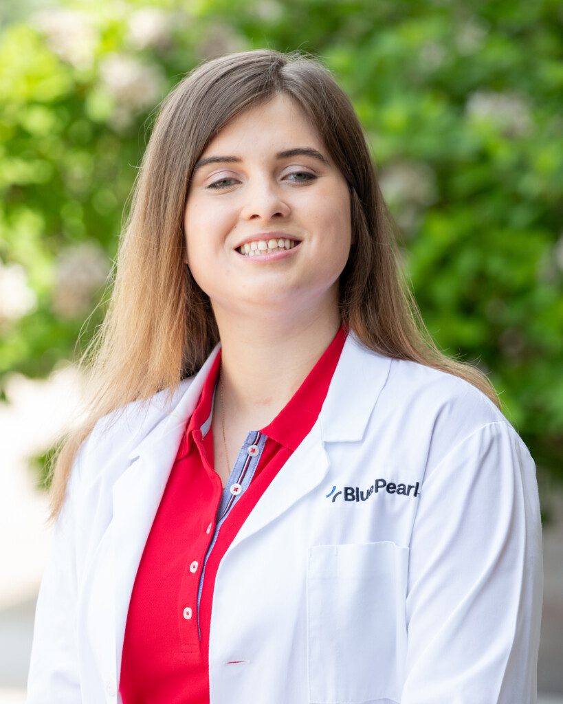 Dr. Urszula Wisniewska standing outside in front of a tree, smiling and in her white coat.