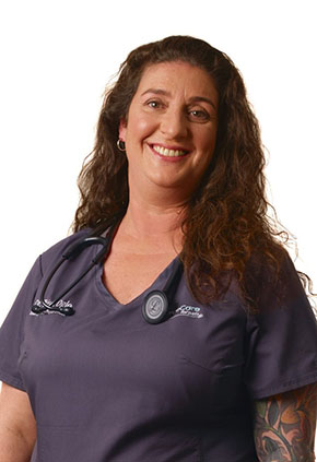 Dr. Trish Ogle smiles for a professional headshot. She is wearing blue-grey scrubs and has a stethoscope around her neck.