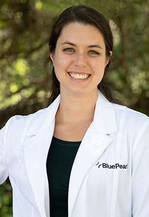 Dr. Emma Clark outside smiling. She has on her BluePearl white coat and a black top with her right hand on her hip.