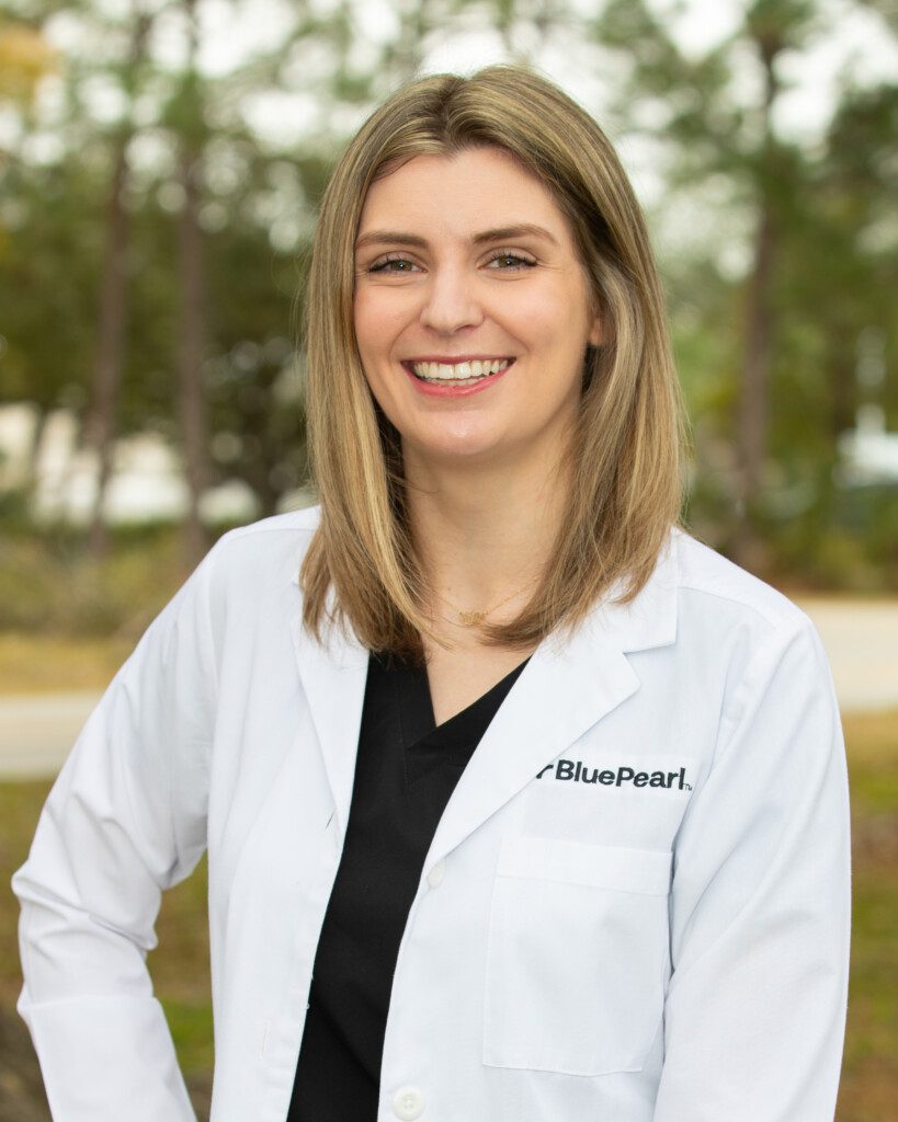 Dr. Sarah Smith smiling outside in her BluePearl white coat and a black top. She has her right hand on her hip.
