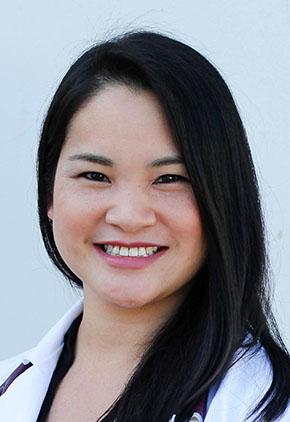 Dr. Kimberly Terry smiles outside for a professional headshot. She is wearing a black top and her white coat. She has a black stethoscope around her neck.