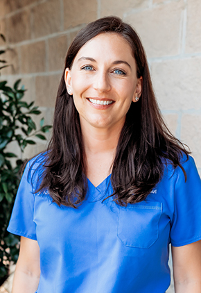 Dr. Aden Hardison smiling outside in front of a brick wall. She has on blue scrubs.
