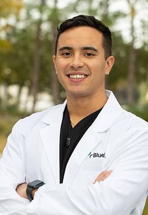 Dr. José Fonseca Martinez outside smiling. He is wearing his BluePearl white coat and a black top. He has his arms crossed with a black watch on his left wrist.