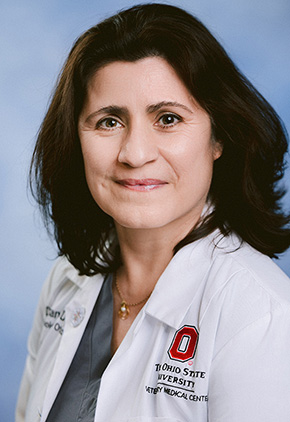 Dr. Sandra Diaz smiling in front of a professional blue background. She is wearing her white coat.