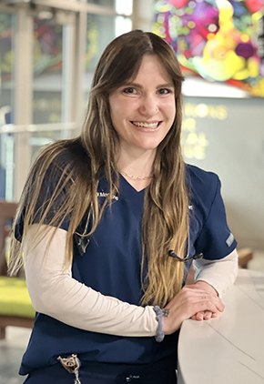 Dr. Jenna Dinstell smiles in the lobby of our Reno hospital. She is leaning against the front desk and wearing navy BluePearl scrubs with a white long-sleeve underneath.