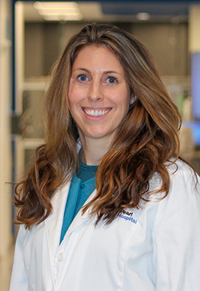Dr. Chelsea Grimes smiling in the lobby of BluePearl Grand Rapids. She has on a teal scrub top and her BluePearl white coat.