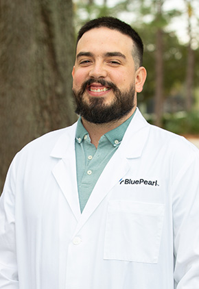Dr. Enrique Gomez Peña smiling outside in his BluePearl white coat and green dress shirt.