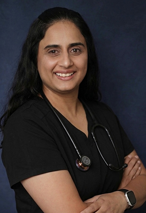 Dr. Tranjot Sran smiles for a professional studio headshot. She is wearing black scrubs and has a stethoscope around her neck.