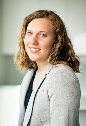 Dr. Casey Sleznikow standing at an angle, looking over her shoulder and smiling. She has on a grey blazer and black top.