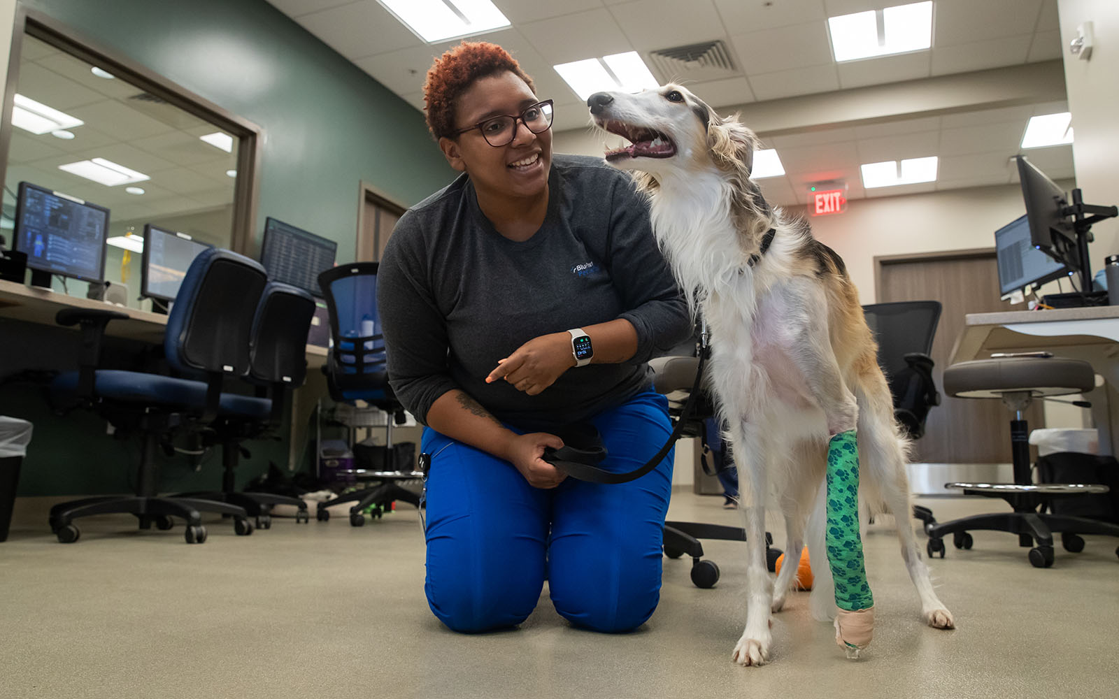 An Associate kneels down next to a white dog wearing a green cast.