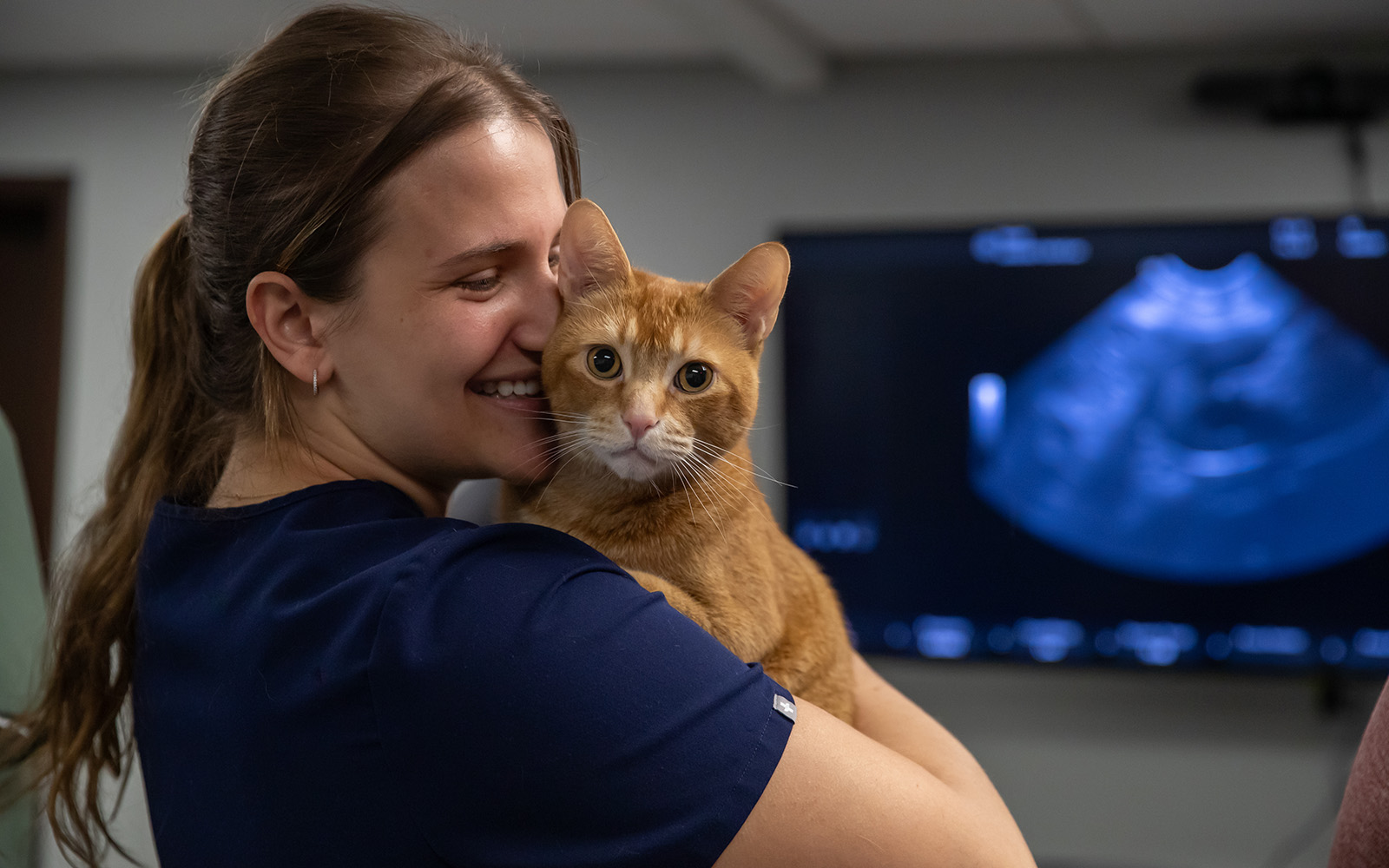 An Associate smiles and laughs while hugging an orange feline patient in her arms.