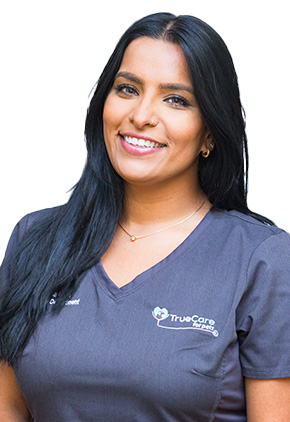 Dr. Nisha Mitra, wearing a charcoal gray scrub top with the TrueCare for Pets logo, smiles in a professional portrait.