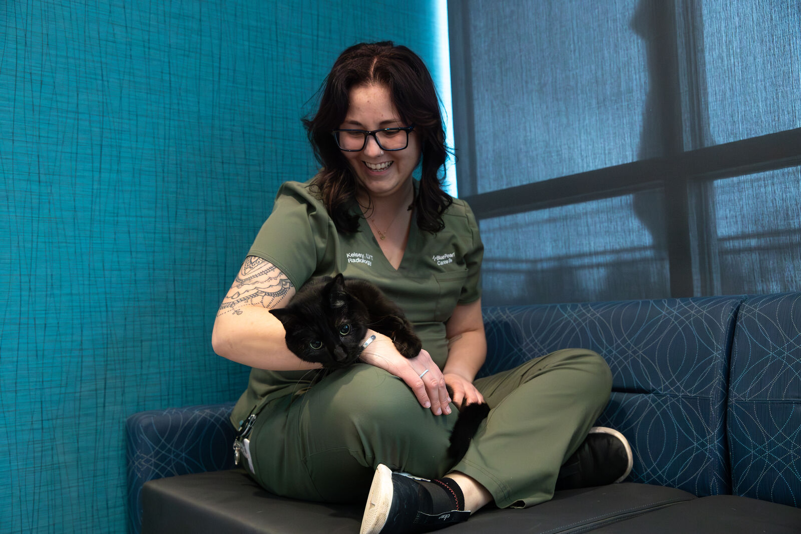 A BluePearl Associate smile as she holds a cat patient in her arms in an animal hospital exam room.