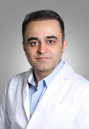 A professional headshot of Dr. Yashar Alami Alamdari in front of a grey background. He is wearing a light blue button-up shirt and his white coat.