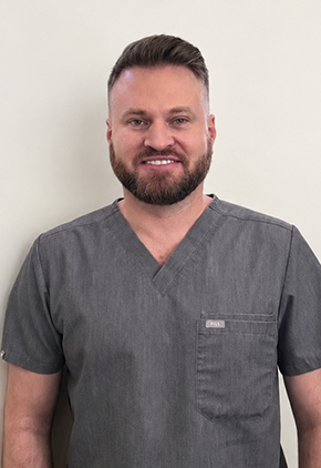 Dr. Daniel Avenick smiles for a headshot in front of a white background. He is wearing charcoal grey scrubs.