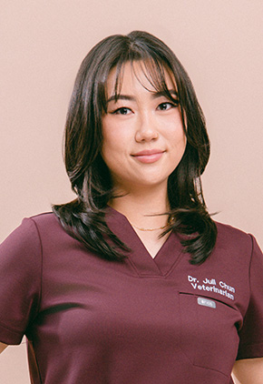 Dr. Juli Chun smiling for a professional portrait in front of a coral background. She is wearing maroon scrubs with her name embroidered on them.