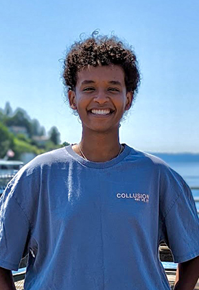 Dr. Kidus Yared smiling outside on a beachfront dock on a sunny day. They have on a blue t-shirt.