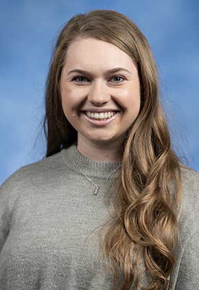 Dr. Meghan McManus smiling for a professional portrait. She is wearing a grey sweater with a small silver necklace.
