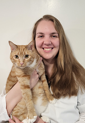 Dr. Lauraine Joensen smiling in front of a white backdrop. She is holding one of her orange cats while wearing her whitecoat.