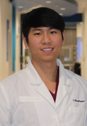 Dr. Ivan Fan smiles for a headshot in the lobby of BluePearl Grand Rapids. He is wearing maroon scrubs and his whitecoat.