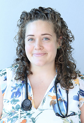 Dr. Gabrielle Robbins smiling for a professional headshot in front of a white backdrop. She is wearing a white dress shirt that features blue, orange and green watercolor tropical flowers. She has a stethoscope around her neck.