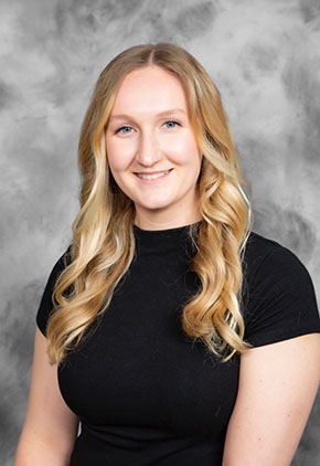 Dr. Haleigh Wright smiles for a professional headshot in front of a grey marbled backdrop. She is wearing a high-neck black top.