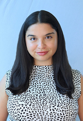 Dr. Andrea Gomez-Ortiz smiling for a professional headshot in front of a white backdrop. She is wearing a white, mock turtleneck with black polka dots.