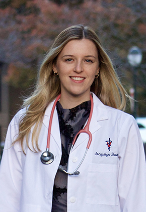 Dr. Jacquelyn Shanley smiling outside. She has on a black top and her whitecoat with a stethoscope around her neck.