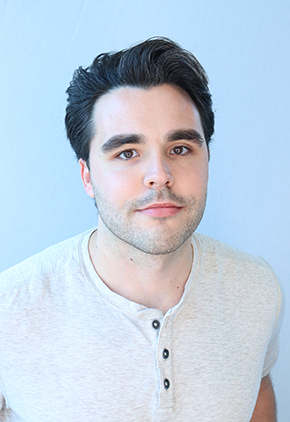 Dr. Kyle Estephan with a soft smile in front of a white backdrop. He has on a light tan, heathered shirt with three buttons.