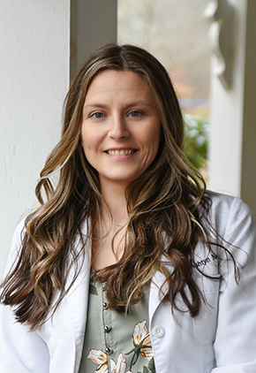 Dr. Ashtyn Neibar smiling outside under an awning. She has on a green floral top and her whitecoat.