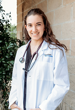 Dr. Cambrie Schumacher smiling outside in front of a brick building. She is wearing her BluePearl whitecoat with a stethoscope around her neck.