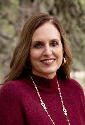 Dr. Leah Tippin smiling outside for a professional headshot. She has on a maroon turtleneck and a long gold necklace.