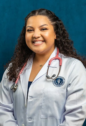 Dr. Jamie Kristen Barnhill smiling for a studio portrait in front of a blue, distressed background. She has on her white coast with a pink stethoscope around her neck.