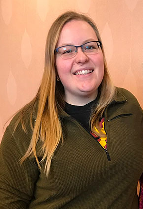 Dr. Lara Stephens-Brown smiles in a conference room. She is wearing an olive-green quarter-zip.