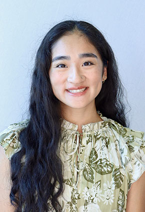 Dr. Mika Tamura smiling for a professional headshot in front of a white backdrop. She is wearing a white mock turtleneck which is featuring green leaves and flowers.