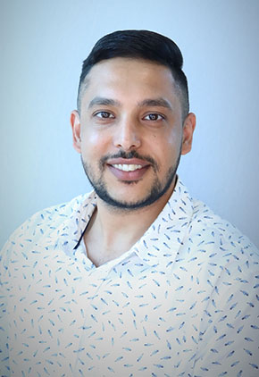 Dr. Navroop Lally smiling for a professional headshot. He is wearing a white patterned dress shirt.