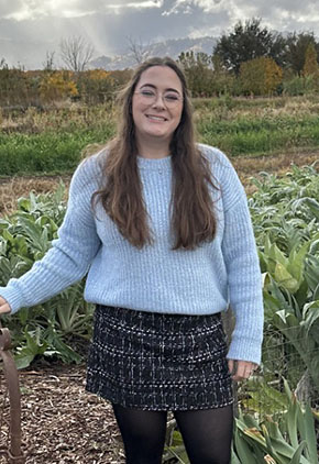 Alysoun Caban, RVT, smiles outside in a rolling field. She is wearing a light blue sweater and a black plaid skirt.