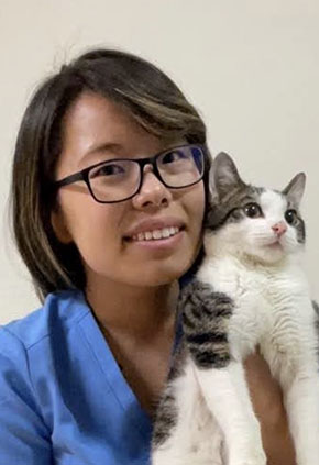 Dr. Molly Mettler smiles while holding up her brown and white cat. She has on blue scrubs.