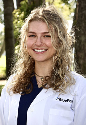 Dr. Hunter Gaias smiles outside in front of trees. She is wearing black scrubs and her BluePearl white coat.