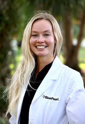 Dr. Cardinal Hastings smiles outside for a professional headshot. She is wearing black scrubs and her BluePearl whitecoat.