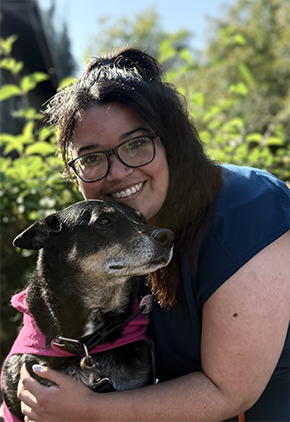 Dr. Bianca Lara smiles outside with her Caribbean rescue dog, Gabby. she is wearing glasses and a navy blue blouse.