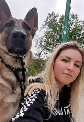 Rebecca Lazok takes a selfie outside with her German Shepherd. She is wearing a black hoodie with a white checkerboard patter on the sleeves.