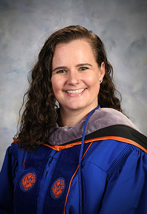 Dr. Dani LaBonte smiles for her DVM graduate photo in front of a grey studio background. She has on her blue and orange University of Florida doctoral robe.