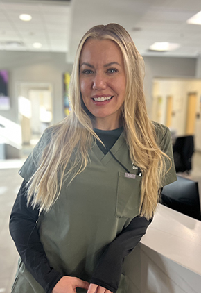 Dr. Anna Bank smiles for a professional headshot inside the lobby of BluePearl Reno. She is wearing olive green scrubs with a navy long-sleeved t-shirt underneath.