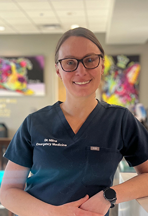 Dr. Christina Milne smiles in the lobby of our Reno hospital as she leans on the front desk. She is wearing navy BluePearl scrubs.