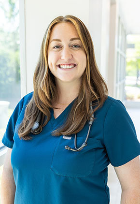 Dr. Jessica Hayes smiles for a headshot in the lobby of BluePearl Pet Hospital. She is wearing teal scrubs and has a stethoscope around her neck.